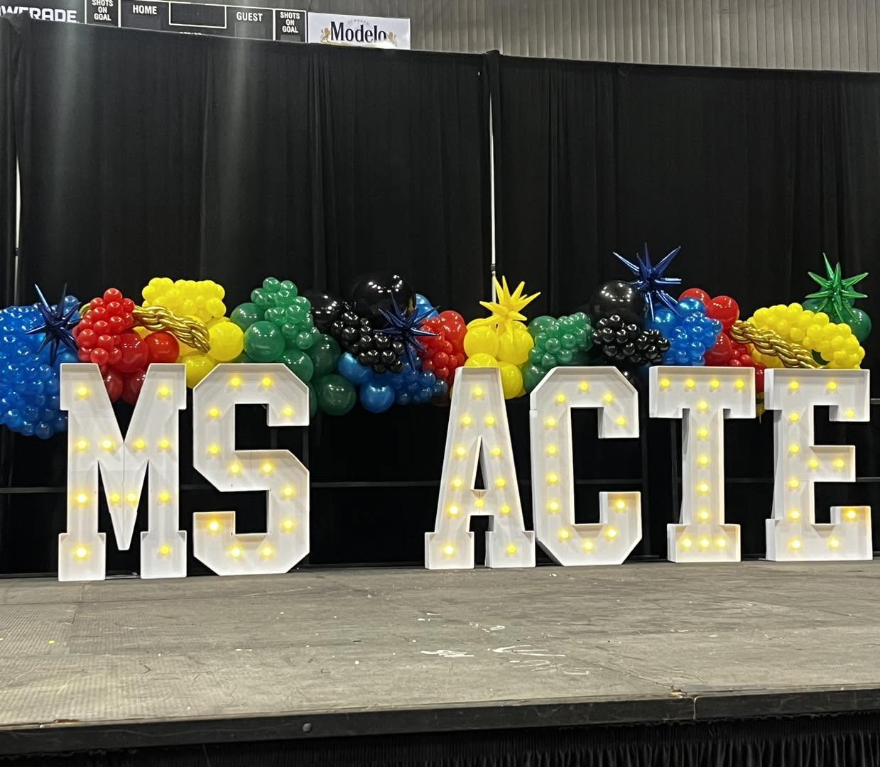 Balloon décor — MS ACTE conference stage letters with colorful balloon accents