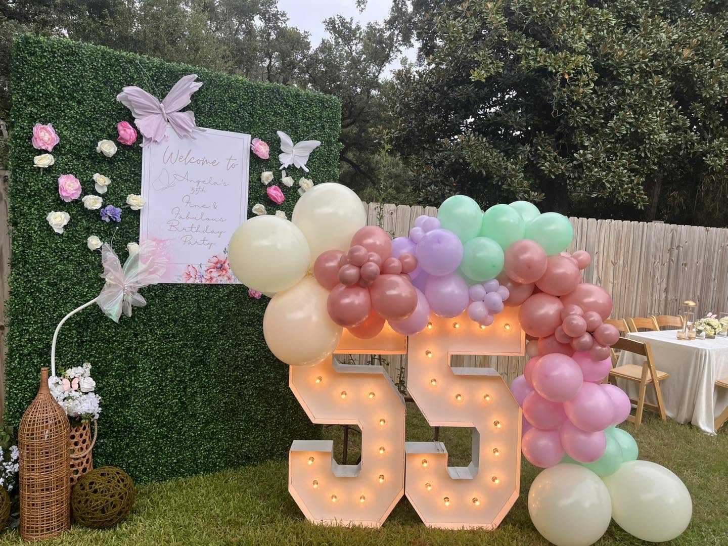 Pastel balloon garland with florals and illuminated marquee numbers on a greenery wall