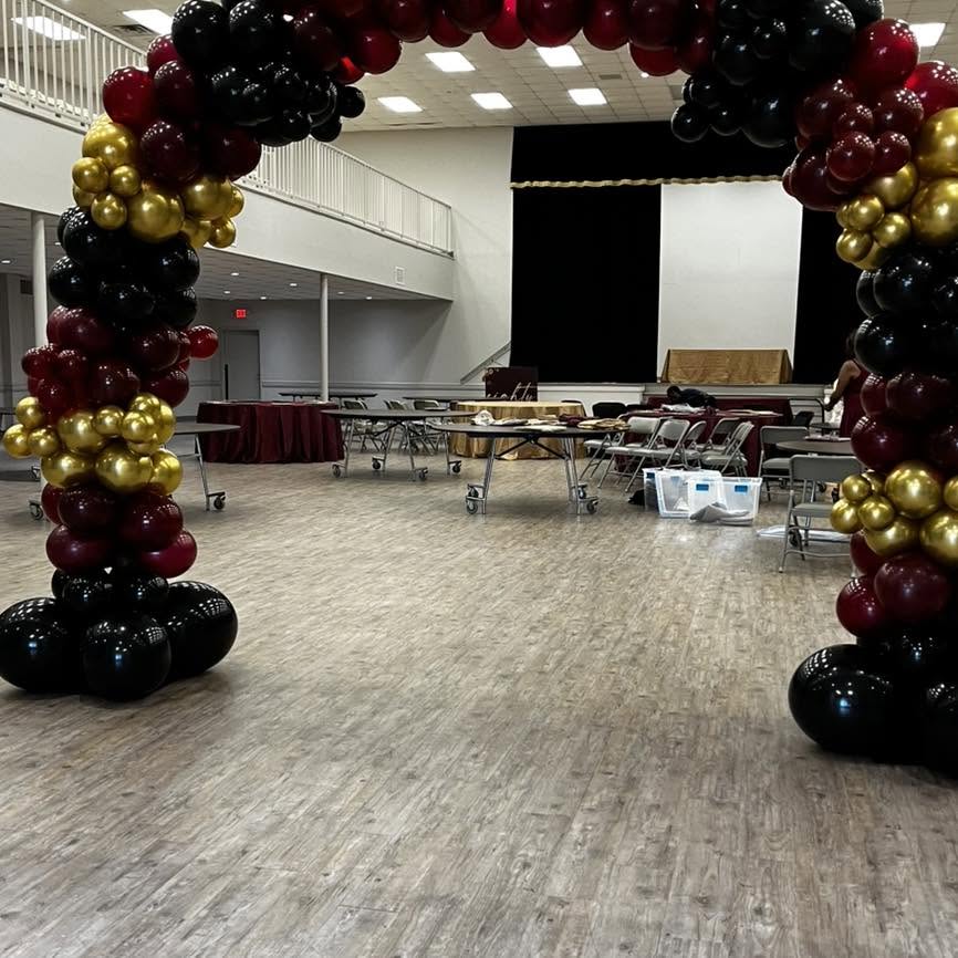 Burgundy, black and gold balloon arch in a banquet hall