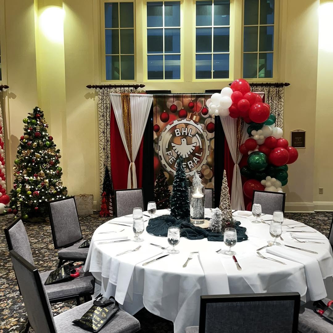 Holiday banquet backdrop with red, green and white balloon garland, draping and decorated trees