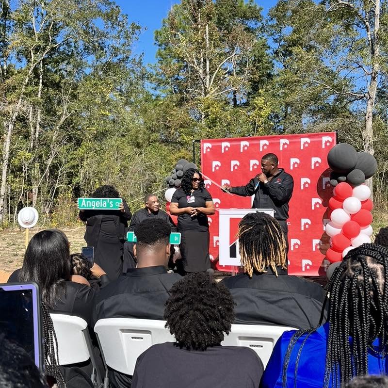 Outdoor ribbon cutting with a red branded backdrop and black, red and white balloon columns